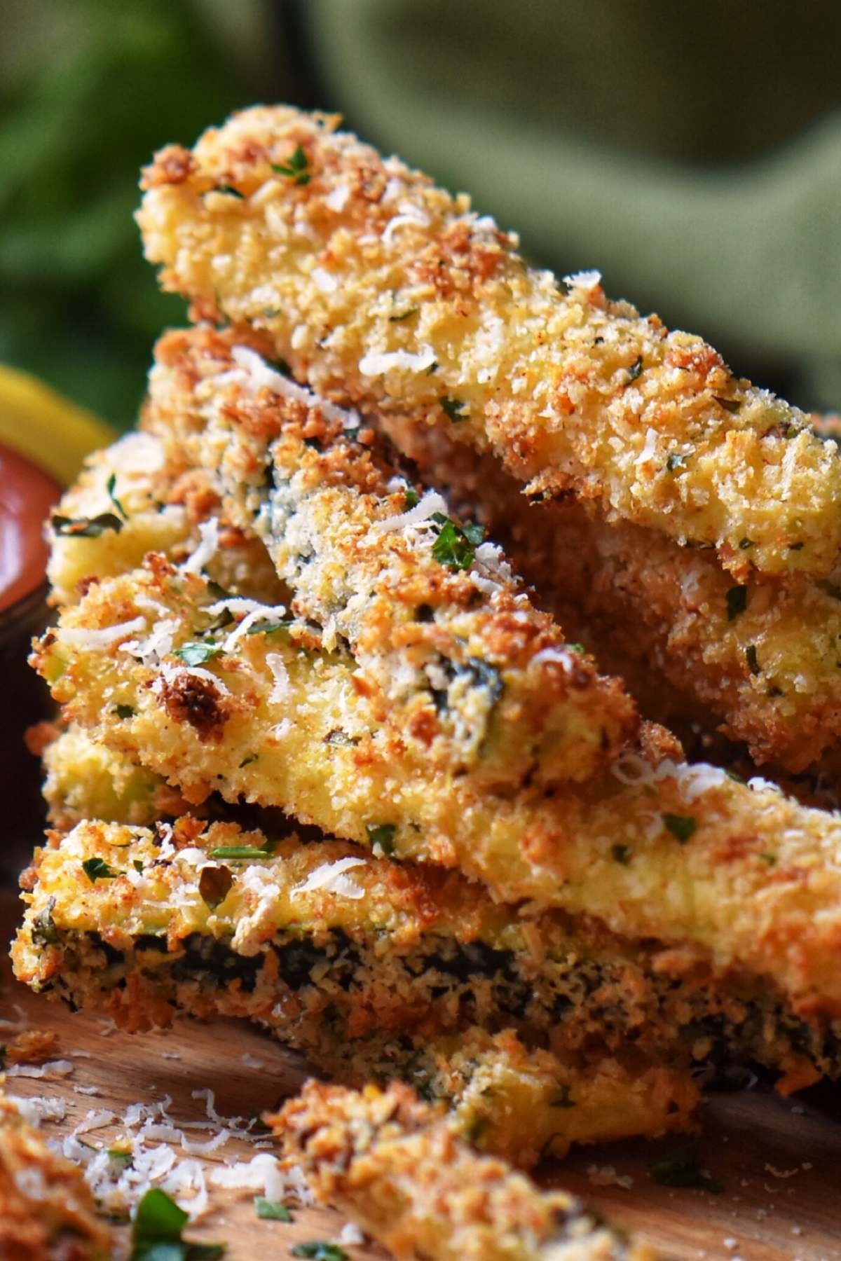 A stack of Air Fryer Parmesan encrusted Zucchini Sticks on a wooden board.