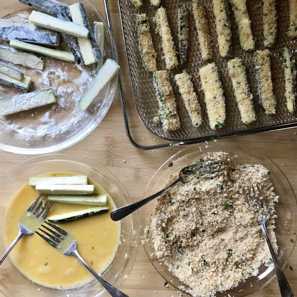 Flour coated zucchini are placed in an egg wash,