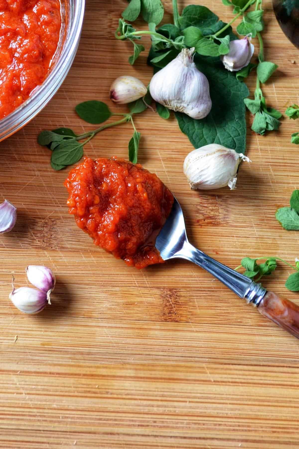 A spoonful of marinara sauce next to garlic cloves.