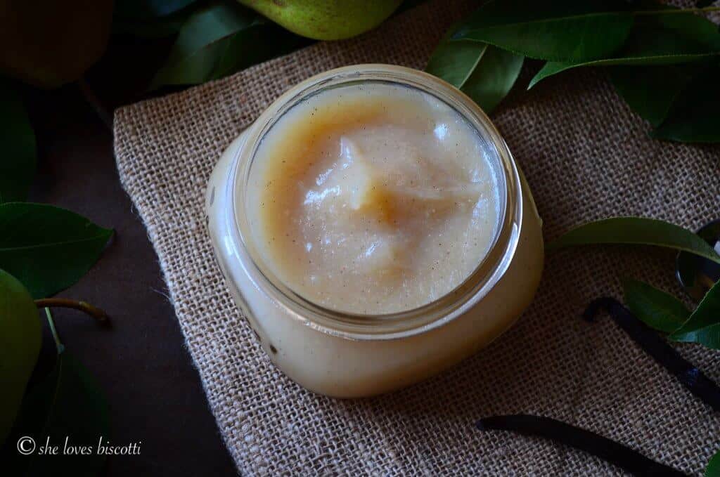 A jar of pear butter, surrounded by fresh pears and vanilla beans.