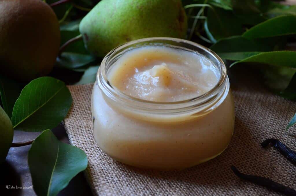 The Vanilla Pear Butter is seen in a wide open canning jar, surrounded by fresh pears. 