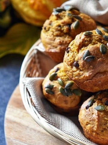 A basket of pumpkin muffins next to squash and mini pumpkins.