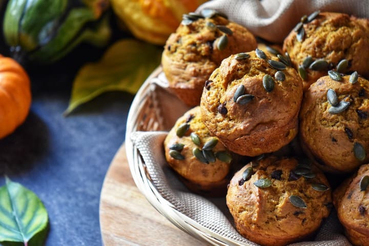 A basket of pumpkin muffins next to squash and mini pumpkins.