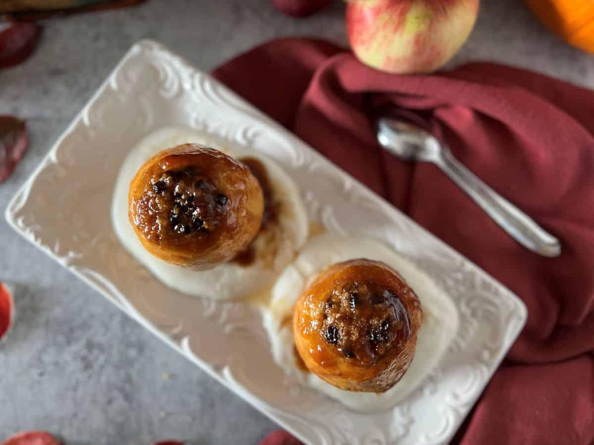 An overhead image of baked apple served on whipped ricotta, drizzled with honey on a white platter.