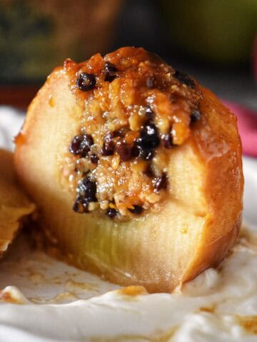 Sliced baked apple with caramelized top showing the warm, spiced oat and currant filling inside.