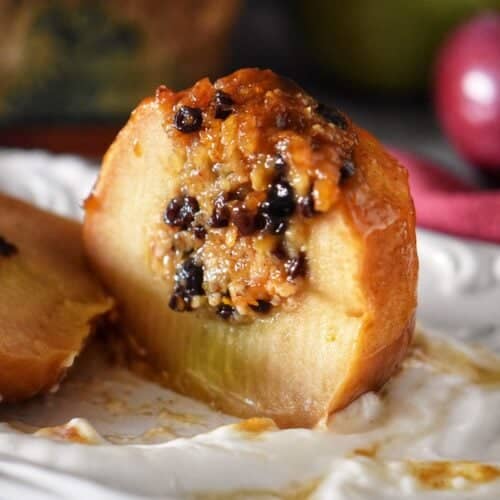 Sliced baked apple with caramelized top showing the warm, spiced oat and currant filling inside.