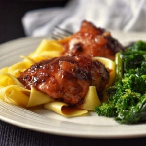 Chicken thighs on a white plate next to rapini and noodles.