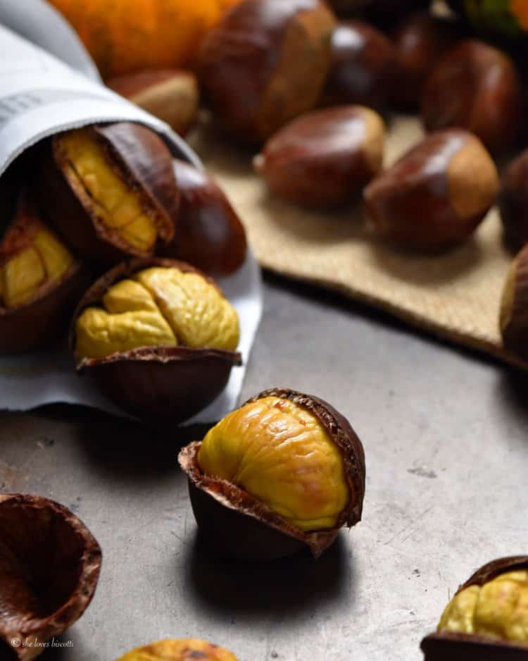 A few oven roasted chestnuts scattered on a steel pan.