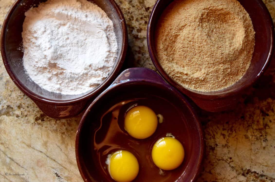 Flour, breadcrumbs and eggs are shown in three shallow bowls to dip the croquettes.