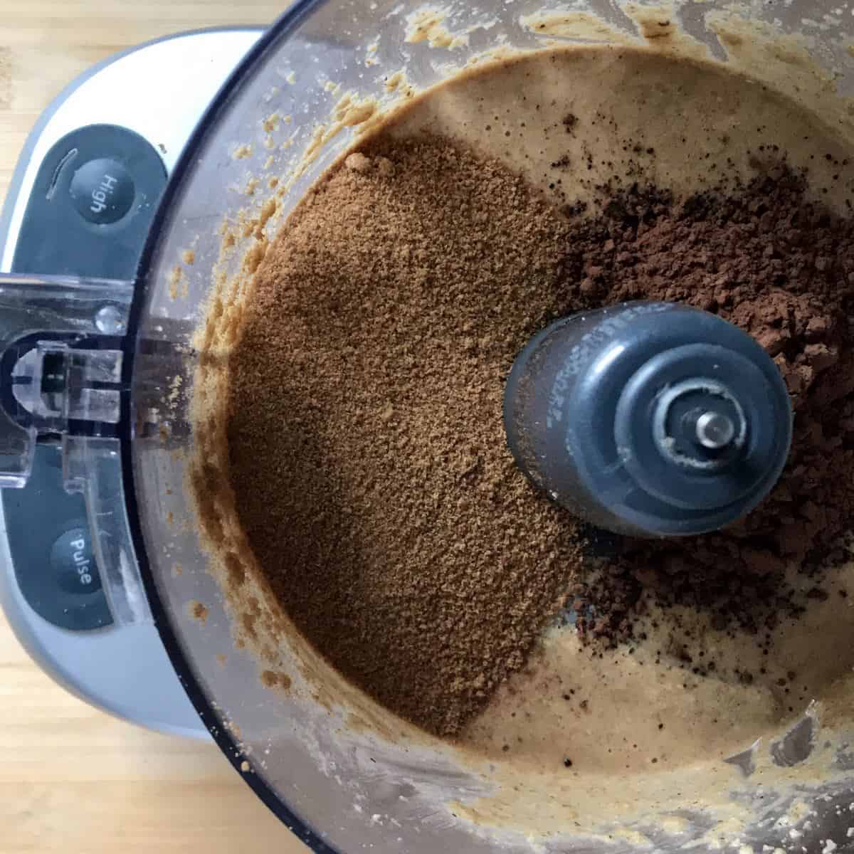 The addition of coconut sugar, cocoa, and salt to hazelnut butter in a food processor. 