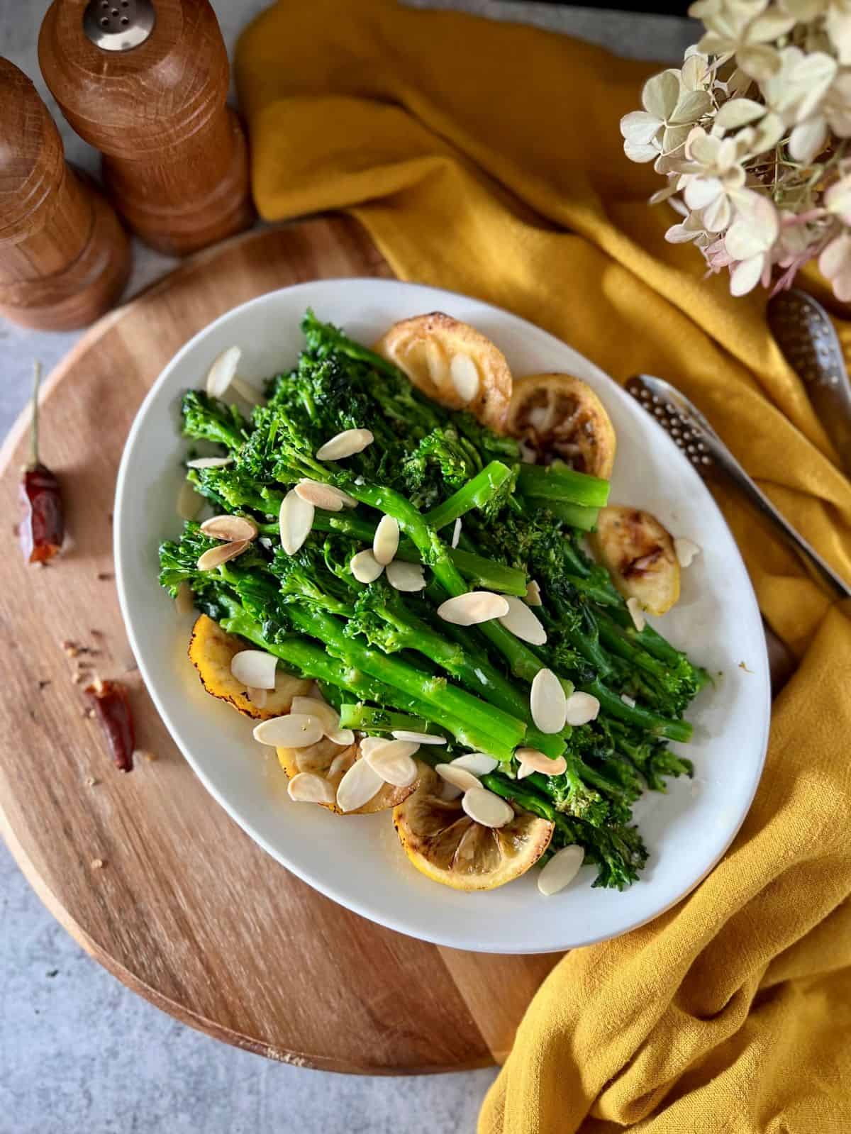 Overhead photo of sauteed garlicky broccolini with toasted almonds and lemon, served on a white dish.
