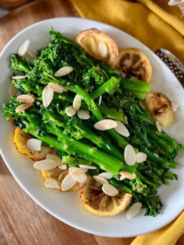 Sauteed broccolini on a white serving platter, garnished with lemon slices and toasted almonds.