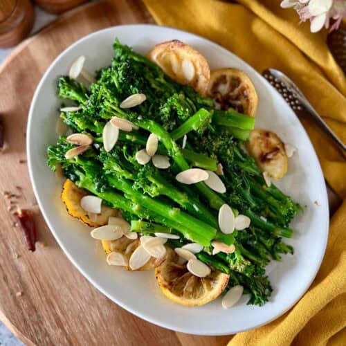 Sauteed broccolini on a white serving platter, garnished with lemon slices and toasted almonds.