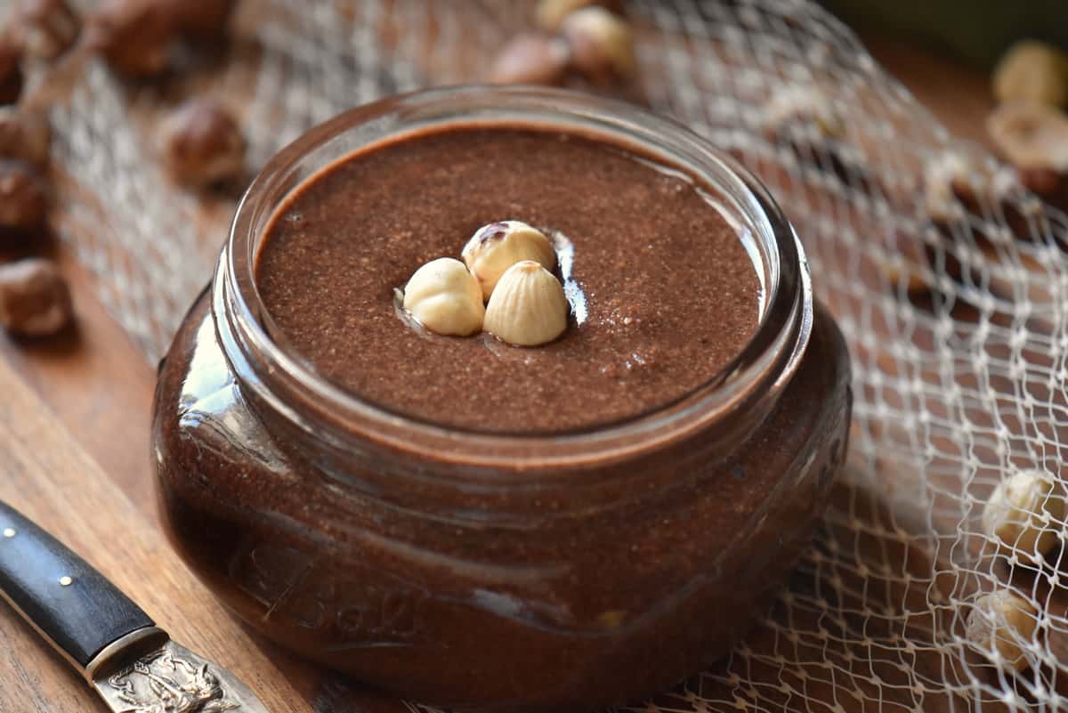 A close up photo of cocoa hazelnut butter in a mason jar on a wooden board.