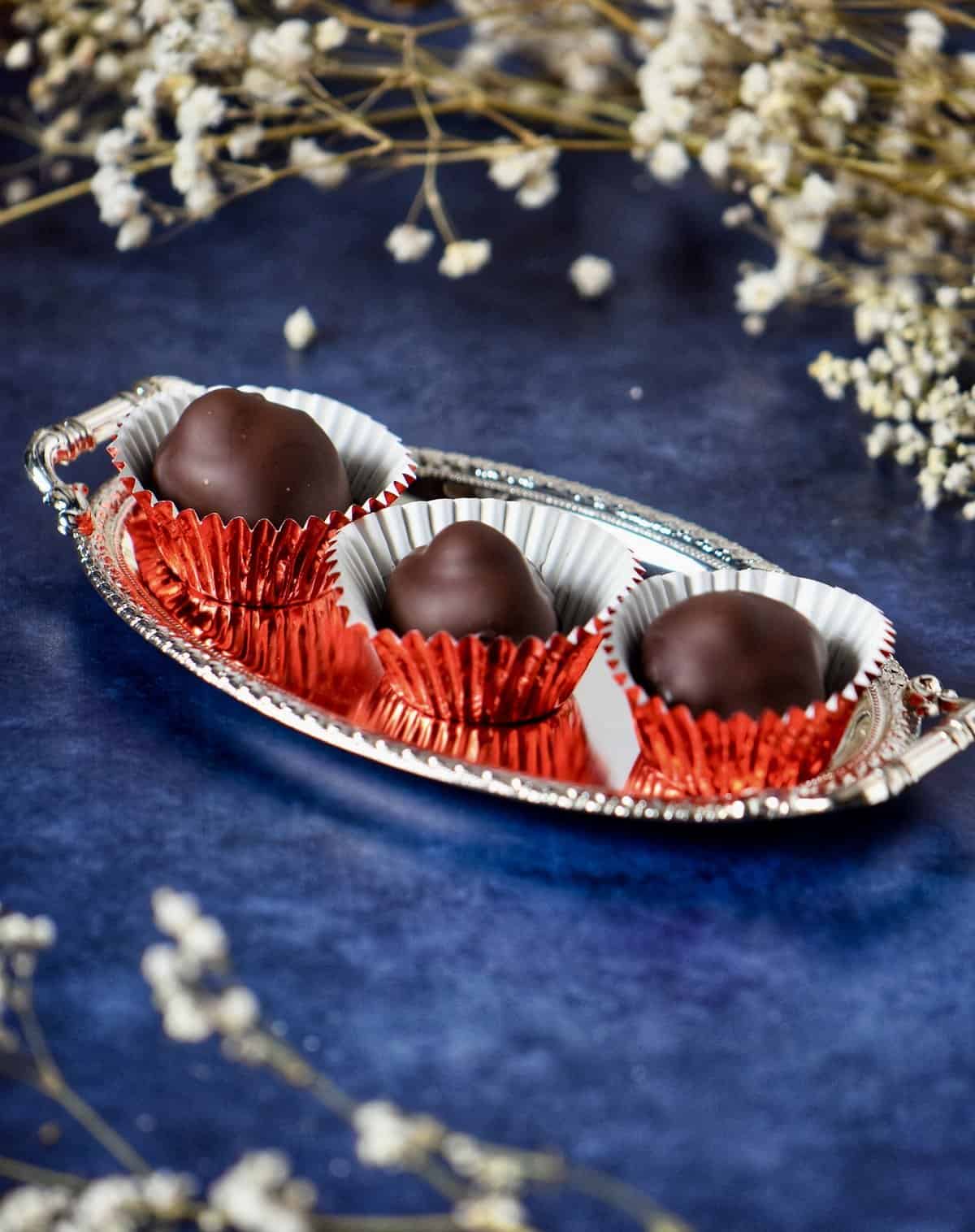 Three homemade baci chocolates in red confection liners on a silver tray.