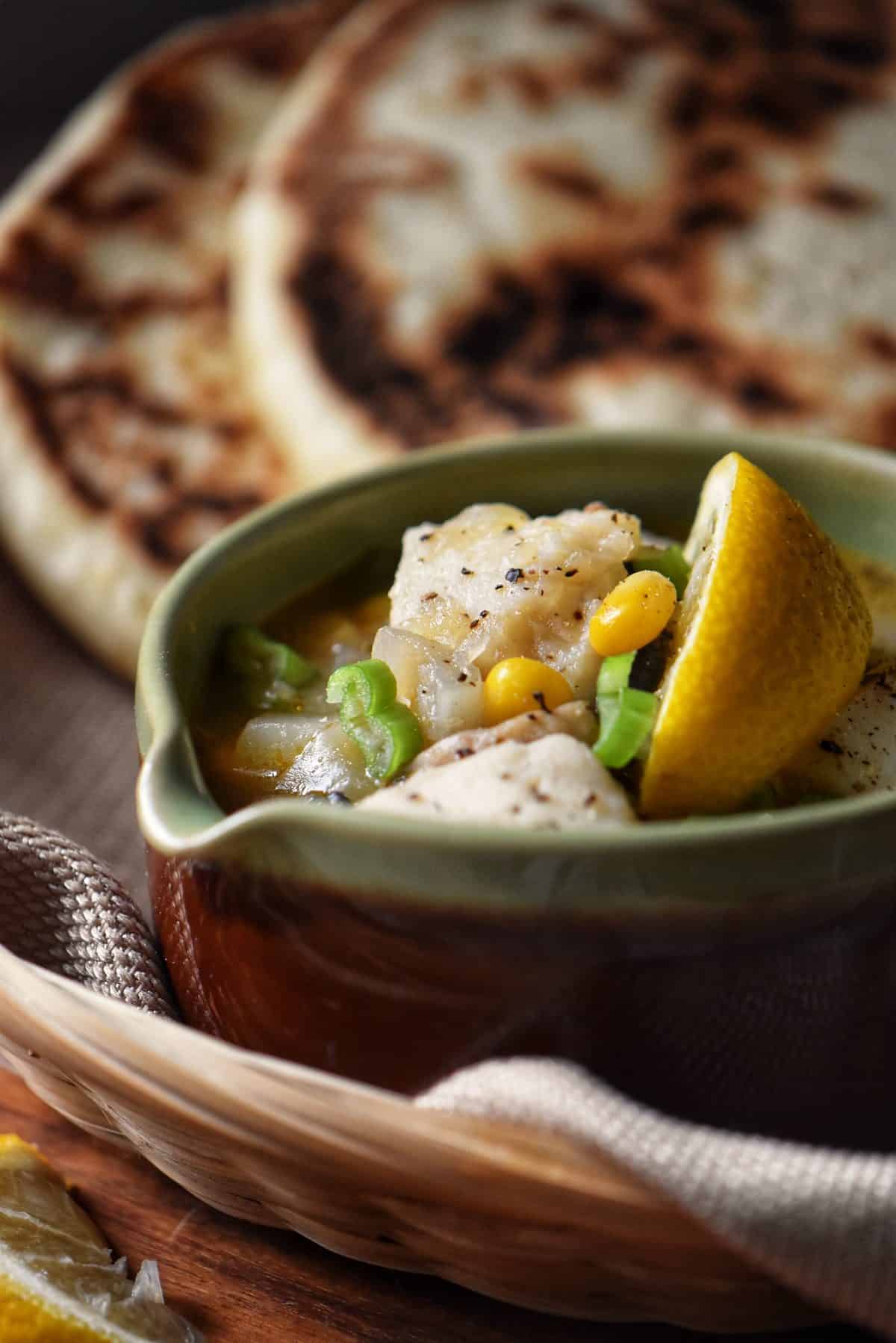A bowl of cod chowder next to naan.