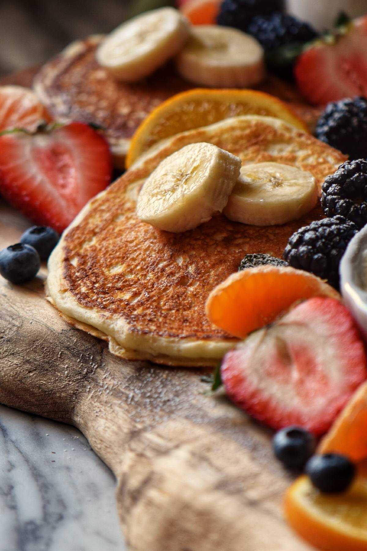 Buttermilk Pancakes surrounded with fresh fruit on a wooden board. 