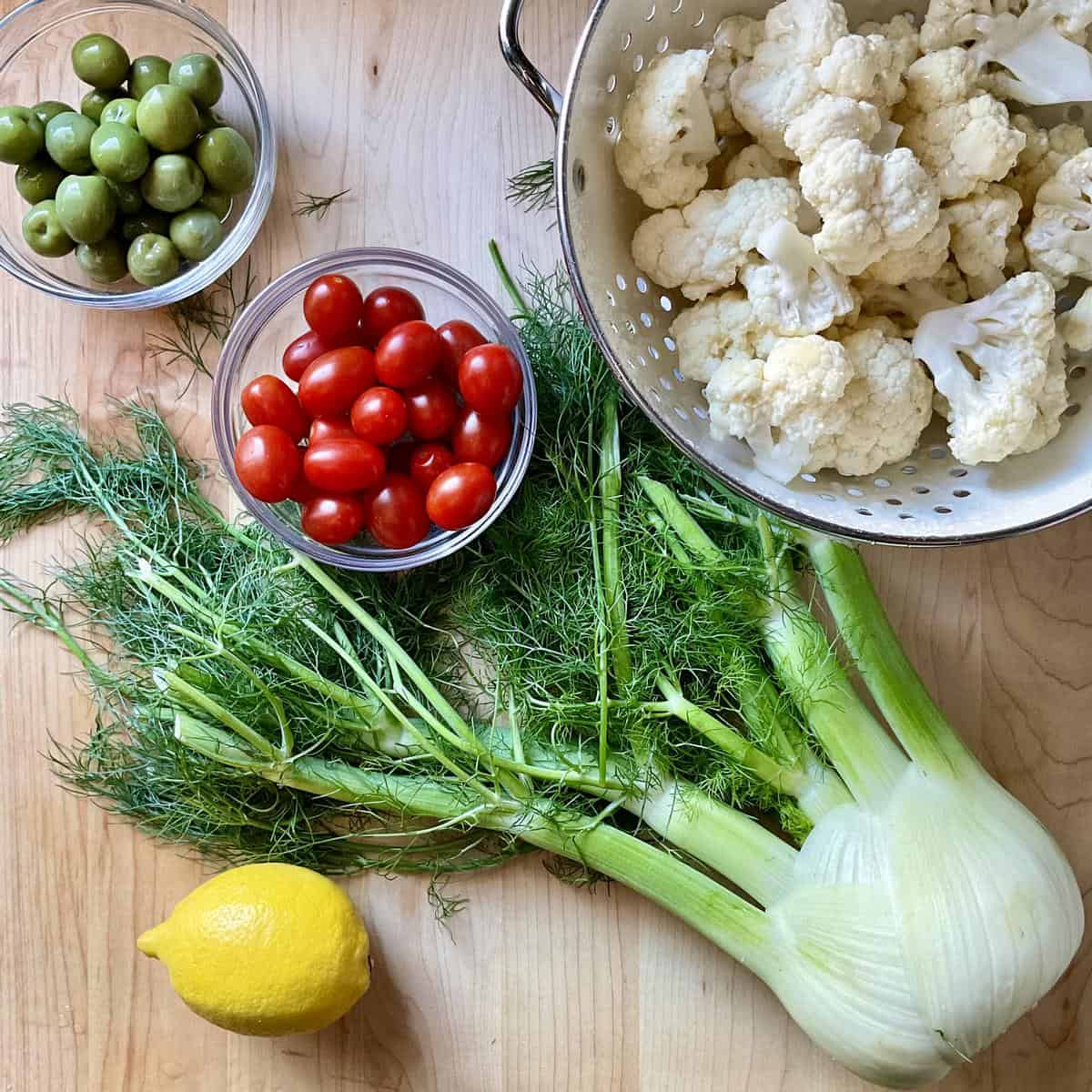 The ingredients to make a cauliflower salad are on a wooden cutting board.