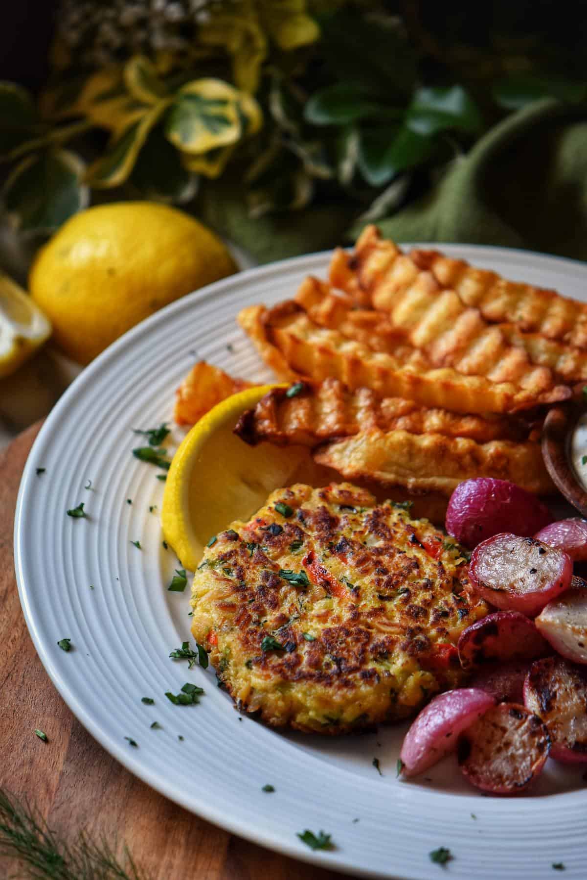A white plate with a tuna patty, crinkle fries and roasted radishes. 