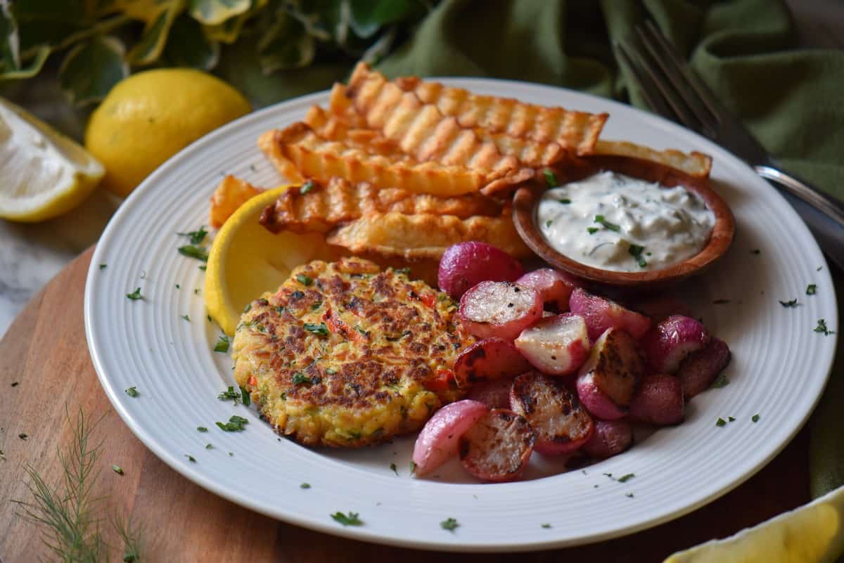 A close up picture of a few Tuna Patties with lemon wedges served on a white oval plate.