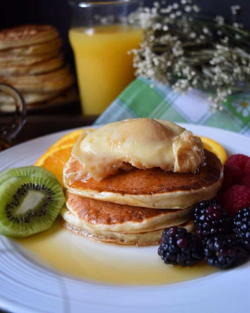 A maple poached egg placed over pancakes, surrounded by fresh fruit.