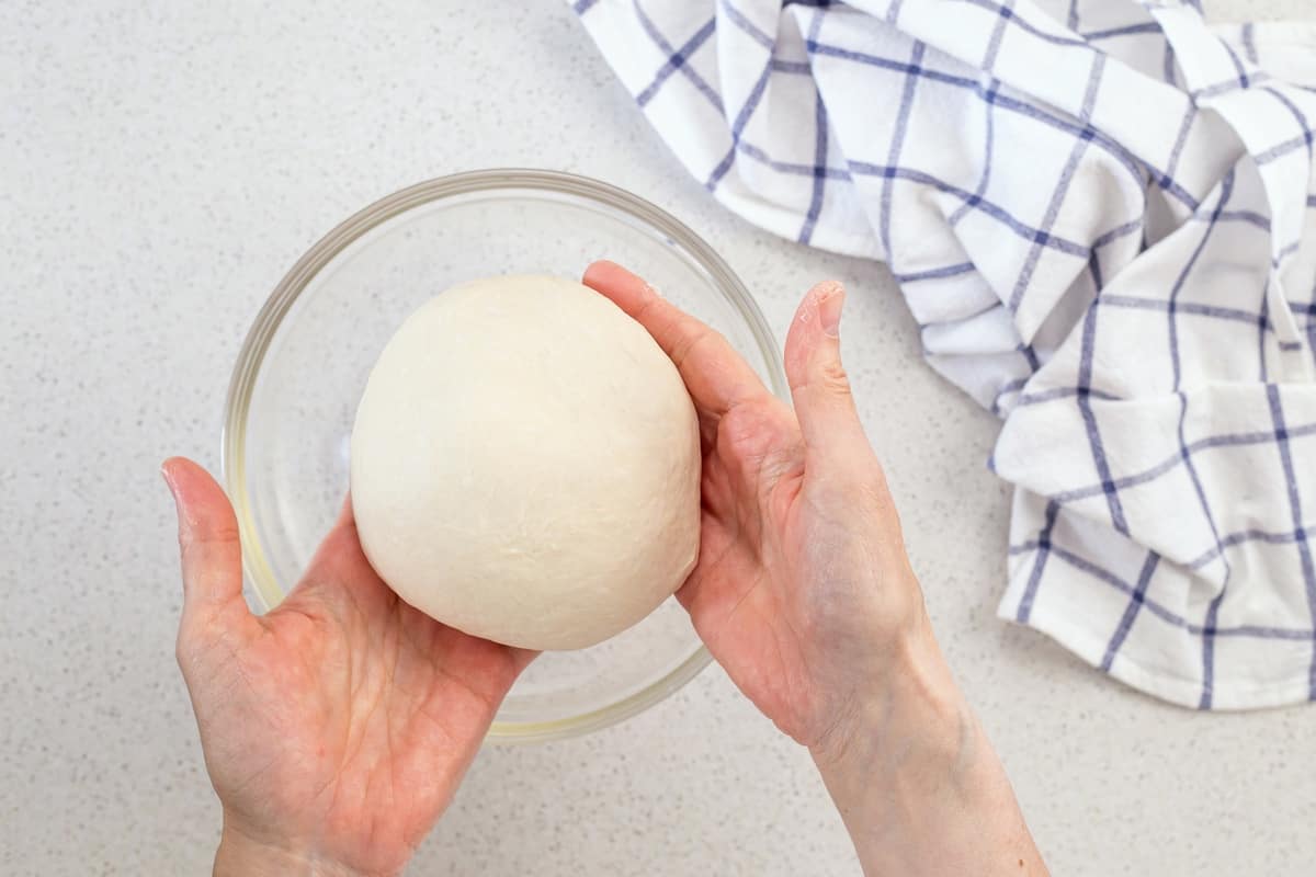 The pizza dough is removed from the stand mixture and is formed into a round ball.