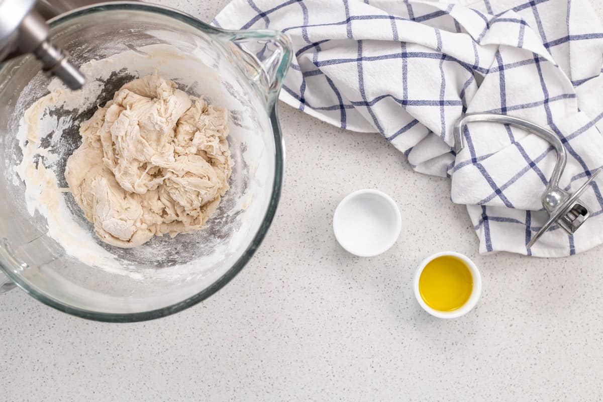 The dough to make pizza is placed in the bowl of a stand mixture.