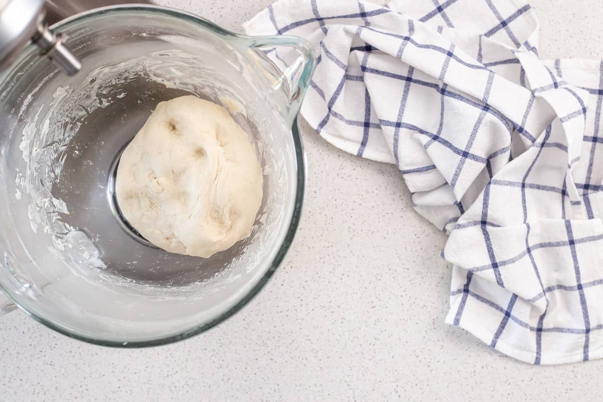 The pizza dough has formed a ball which pulls away from the stand mixture.