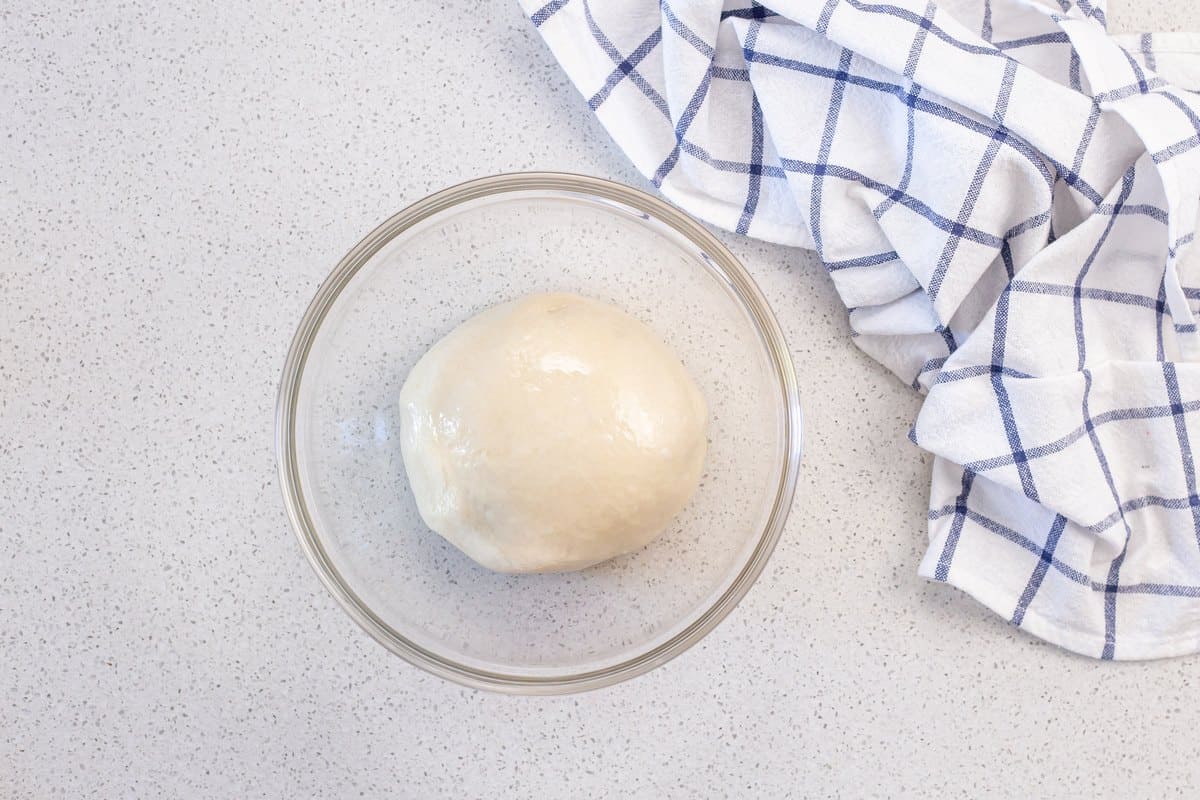 A ball of pizza dough is placed in a lightly greased bowl.