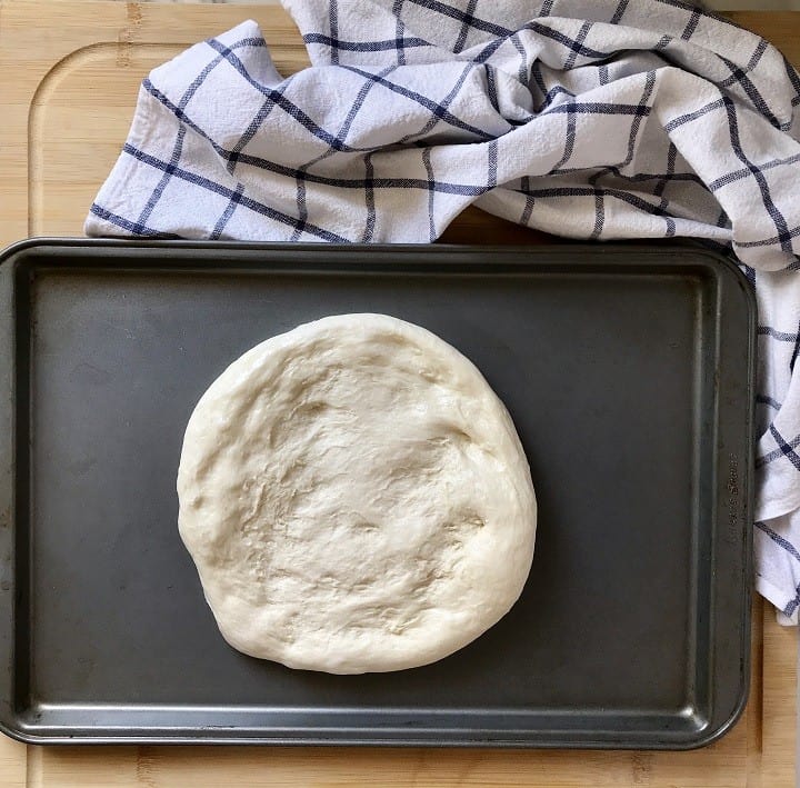 Homemade pizza dough in the process of being stretched on a sheet pan.