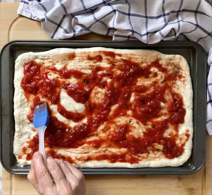 A no cook pizza sauce is being spread on the homemade pizza dough.