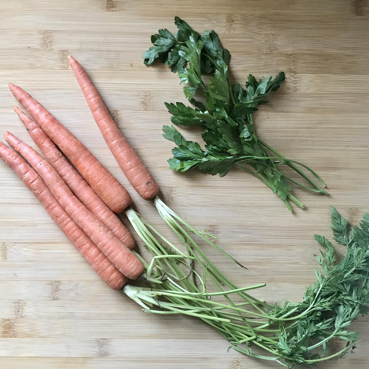 A bunch of carrots and parsley on a wooden board.