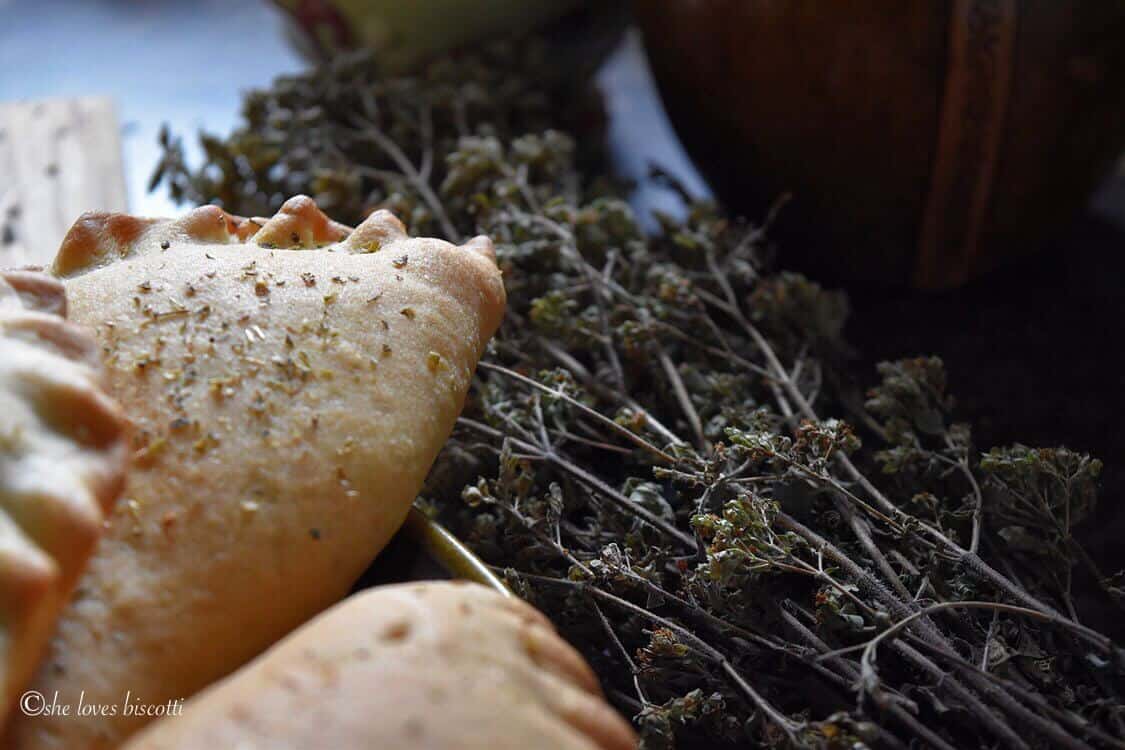 Stems of dried oregano next to calzones.