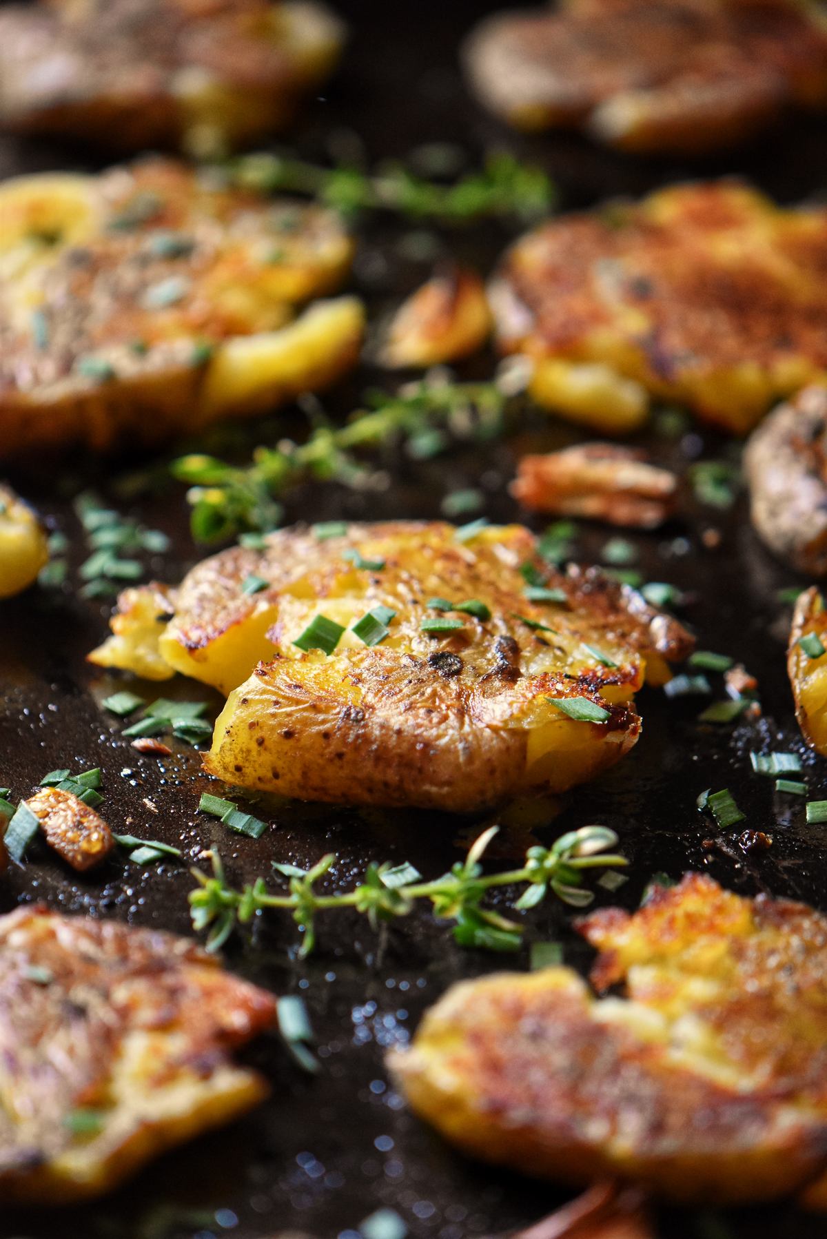 Smashed Fingerling Potatoes garnished with chopped chives on a sheet pan.