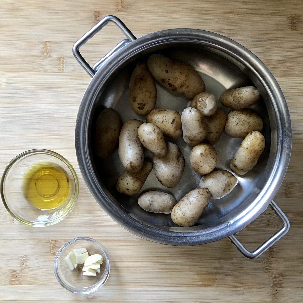 Boiled and drained fingerling potatoes in a pot, next to olive oil and garlic.