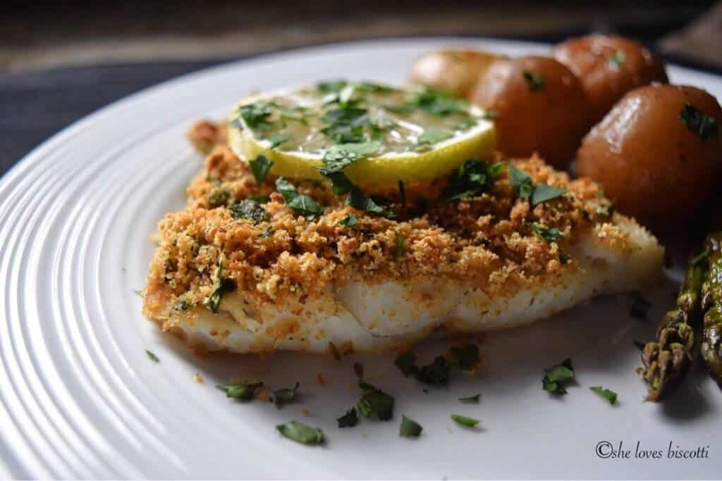 A fish fillet with seasoned breadcrumbs on a white plate.