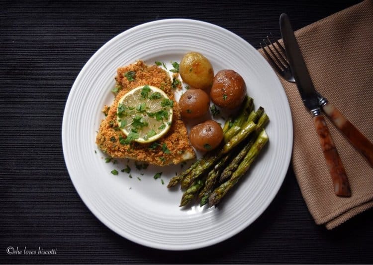 An overhead shot of a plate of baked cod fish, potatoes and asparagus.