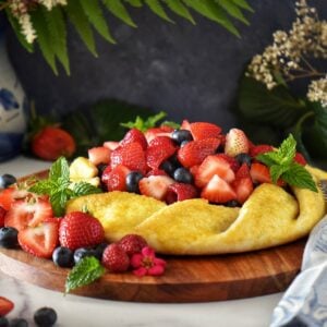 A fruit crostata surrounded by fresh strawberries, raspberries and blueberries.