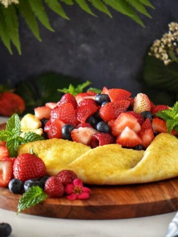 A fruit crostata surrounded by fresh strawberries, raspberries and blueberries.