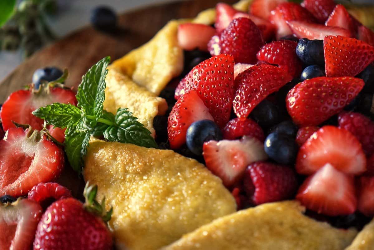 The berry crostata on a wooden board surrounded by fresh berries.