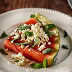 A grilled wateremlon steak topped with feta cheese and basil leaves.