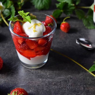 A strawberry Ricotta Parfait in a serving glass surrounded by fresh strawberries.