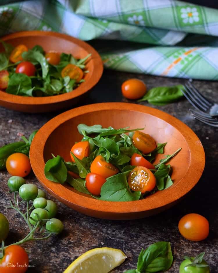 Two wooden bowls filled with arugula cherry tomato salad.