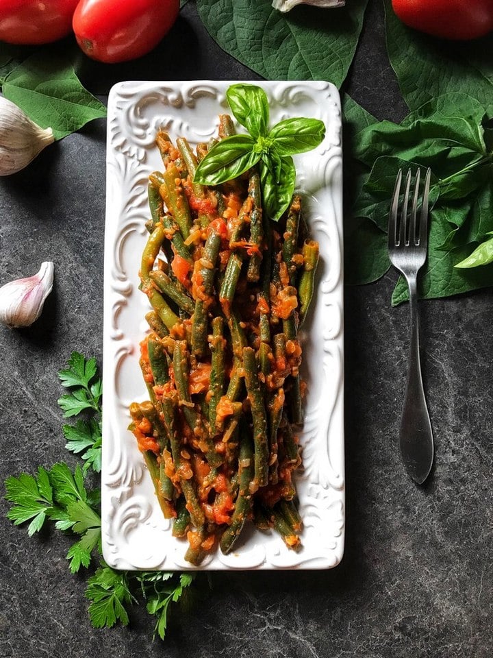 The completed dish of Italian Green Beans in tomato sauce is plated on a white serving dish.