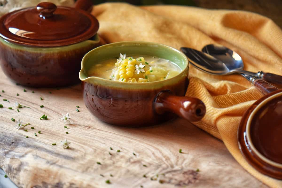 A bowl of corn chowder on a wooden board. 