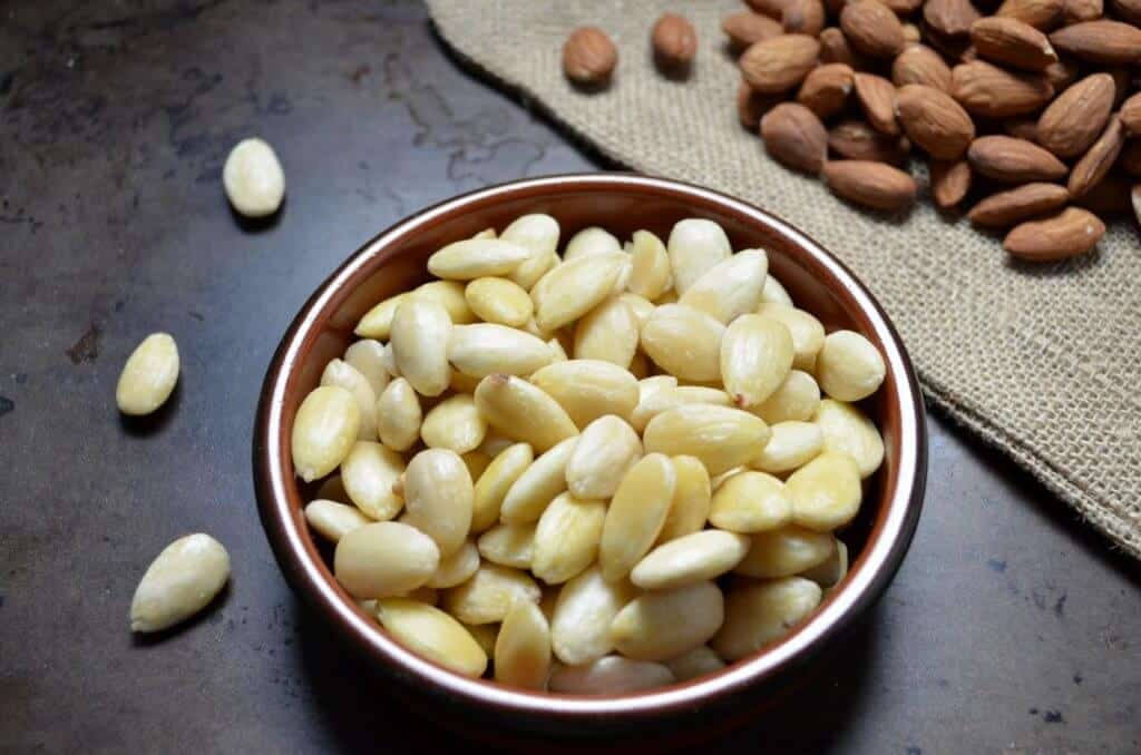 Round dish of blanched almonds with a few almonds on the side.