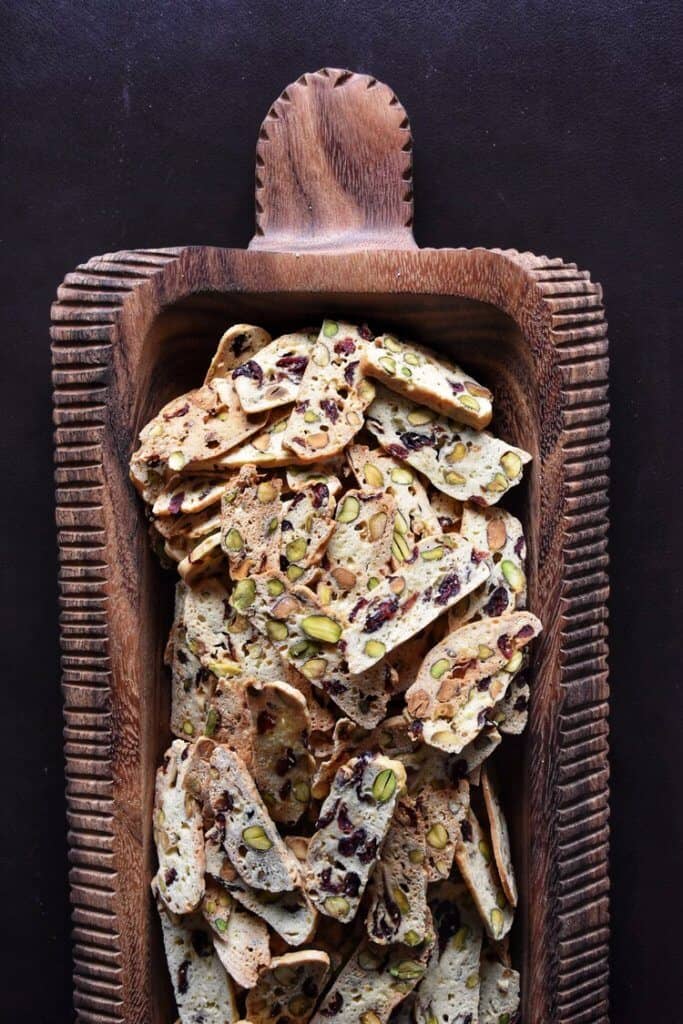 Overhead shot showing thin cranberry pistachio biscotti in a big wooden serving platter.