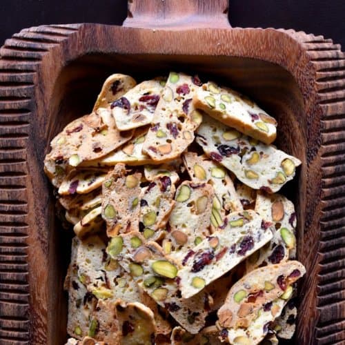 A large decorative wooden serving platter with dozens of thin biscotti.