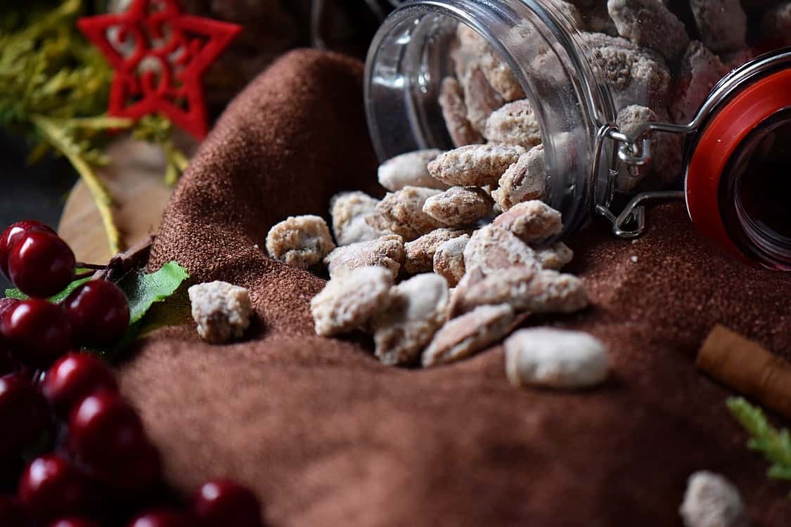 Another picture of the mason jar of Oven Roasted Sugar Almonds spilled on a brown tablecloth.