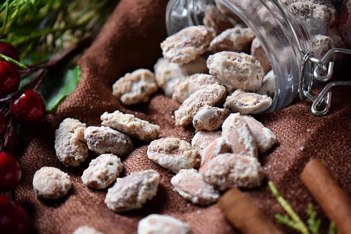 The mason jar of Oven Roasted Sugar Almonds spilled on a brown tablecloth.